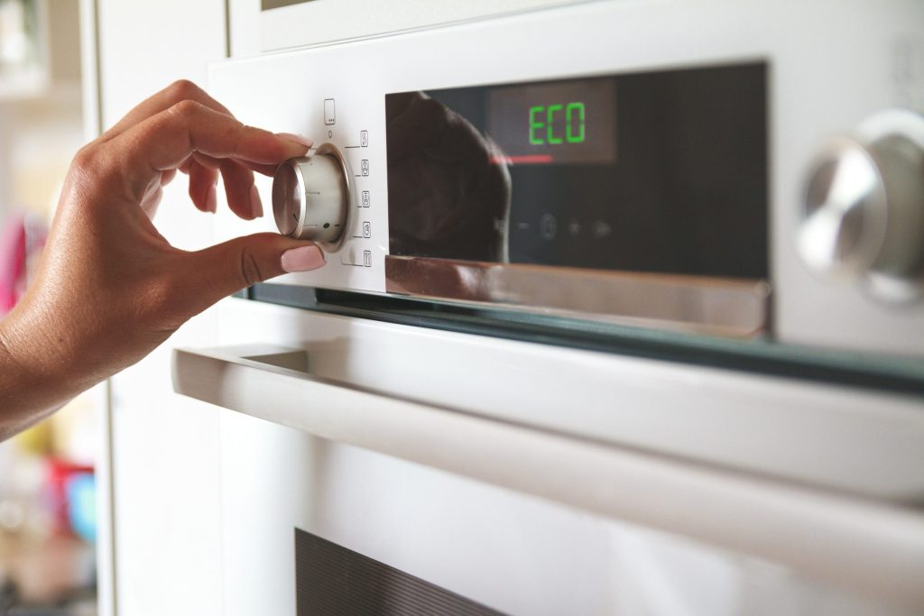 A hand turning the mode dial on a wall oven whose display reads a word rather than a number