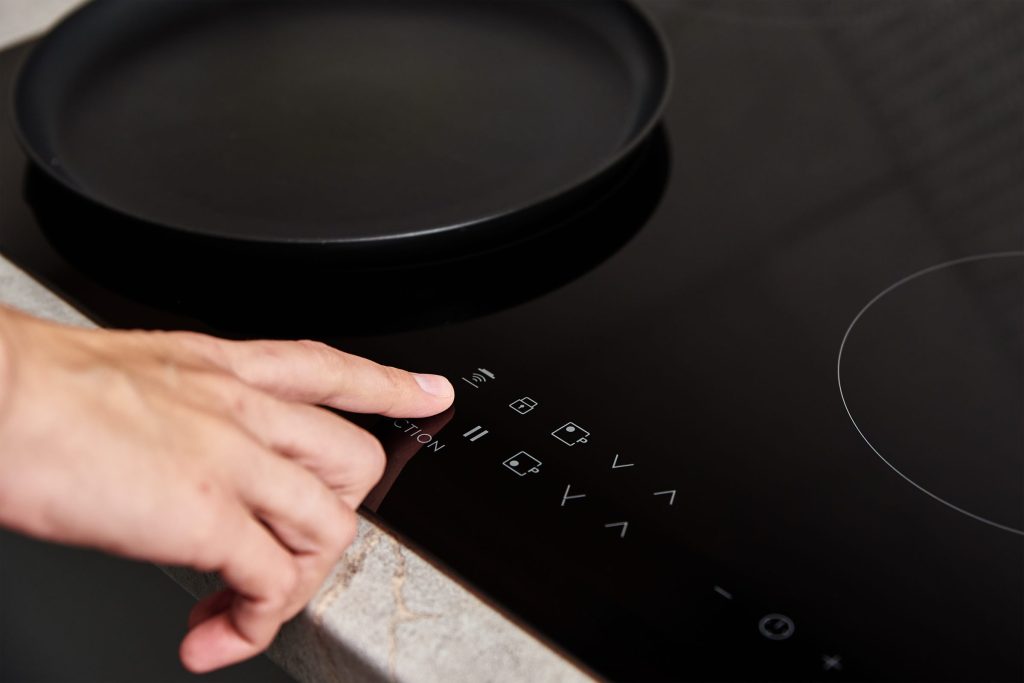 A hand pressing the touch control strip of a black induction cooktop