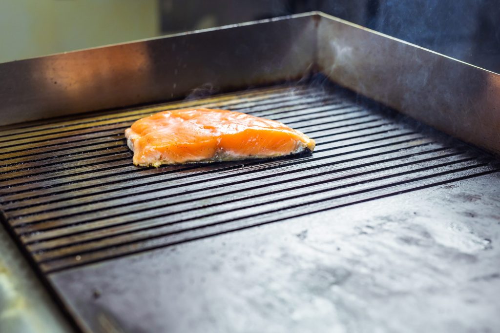 A salmon fillet cooking on the flat steel griddle plate of a range deck