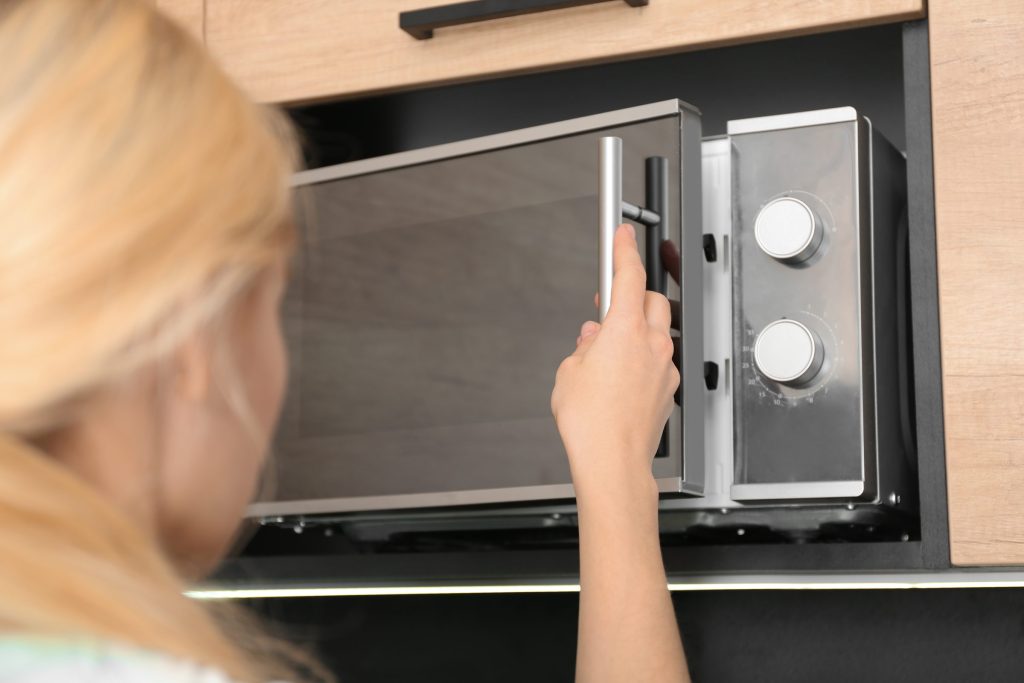 A woman opening the door of a microwave built into a low cabinet run