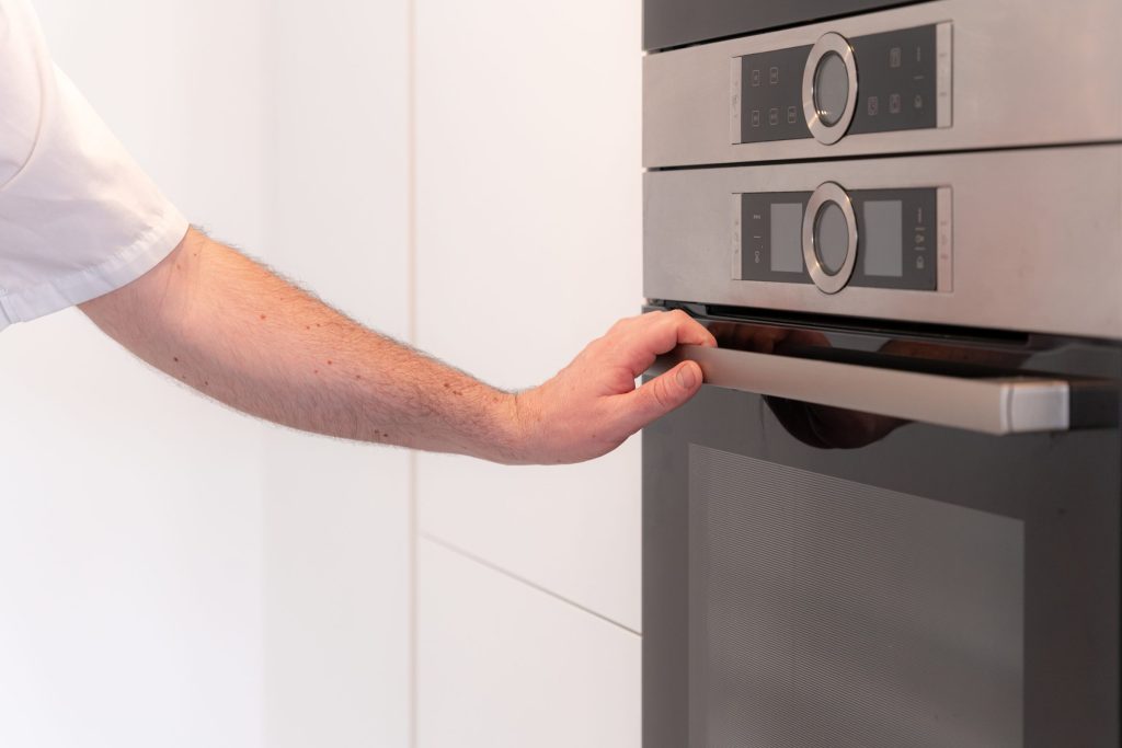A hand on the handle of a built-in appliance below a microwave in a white column