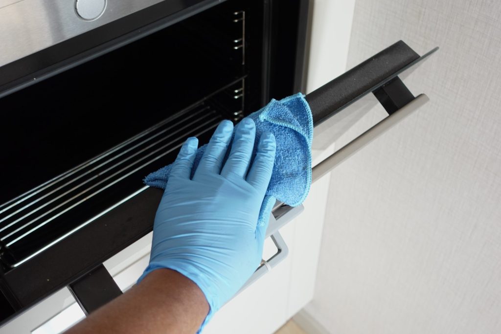 A gloved hand cleaning the inside of an oven with a microfiber cloth.
