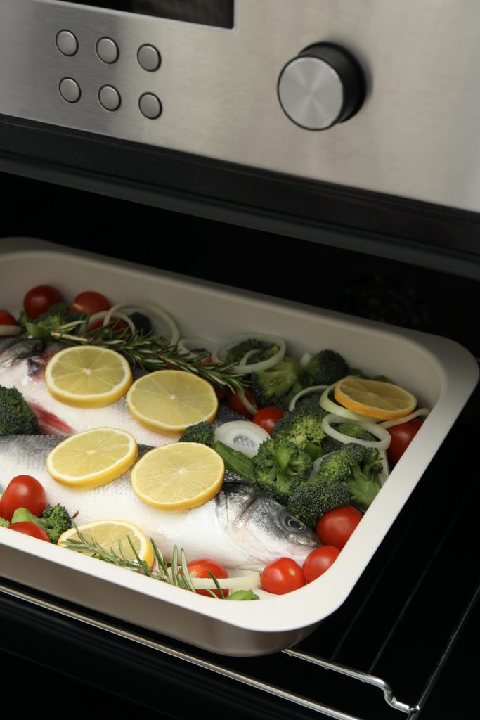 A tray of fish and vegetables in a built-in oven under a lit control panel