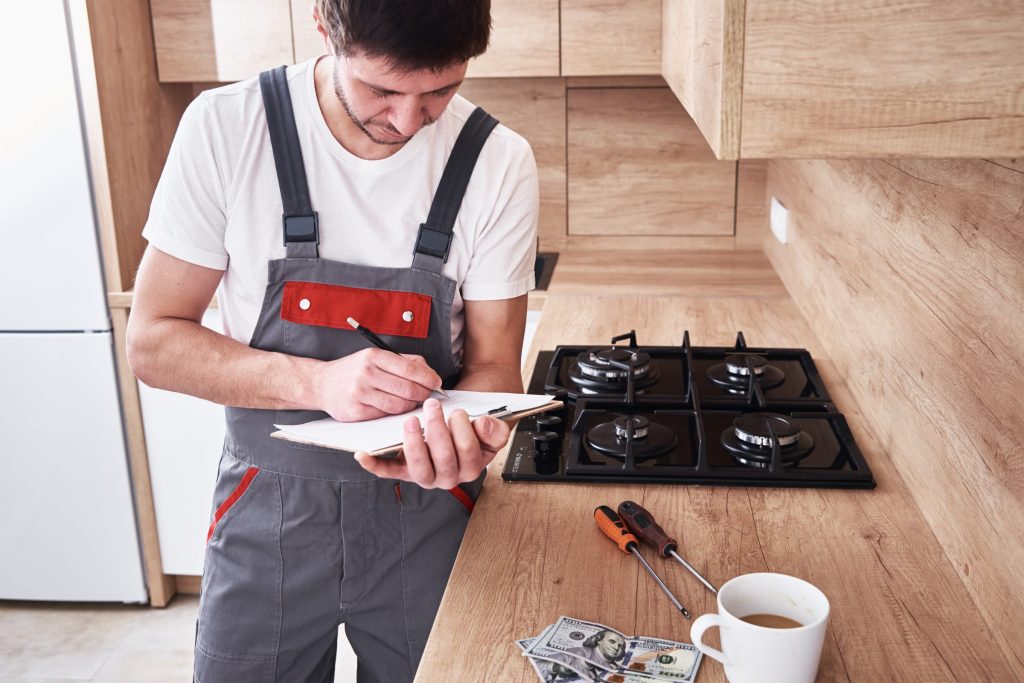 A technician writing on a clipboard beside a gas cooktop.