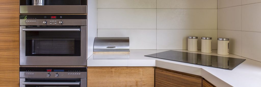A stainless microwave and oven stacked in a wood cabinet run, displays lit red