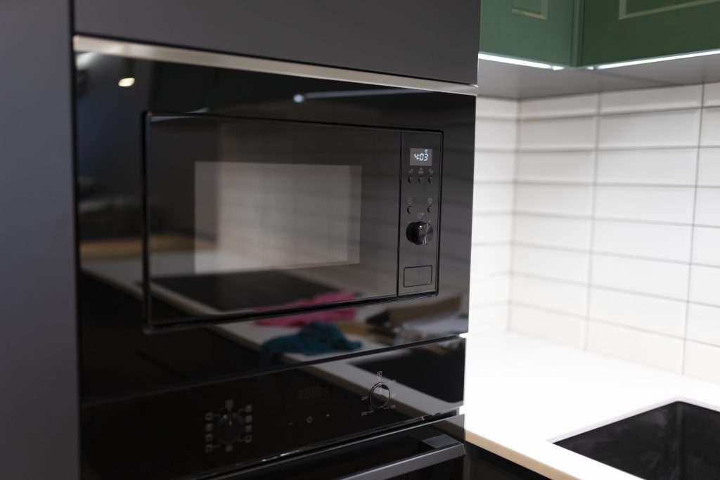 A black built-in microwave above an oven in a tiled kitchen