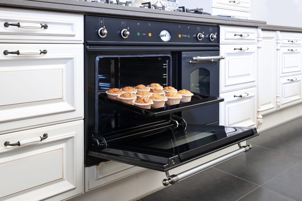 A black built-in oven standing open with a tray of buns on the rack