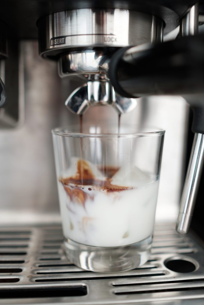 Espresso running from a machine into a glass of milk