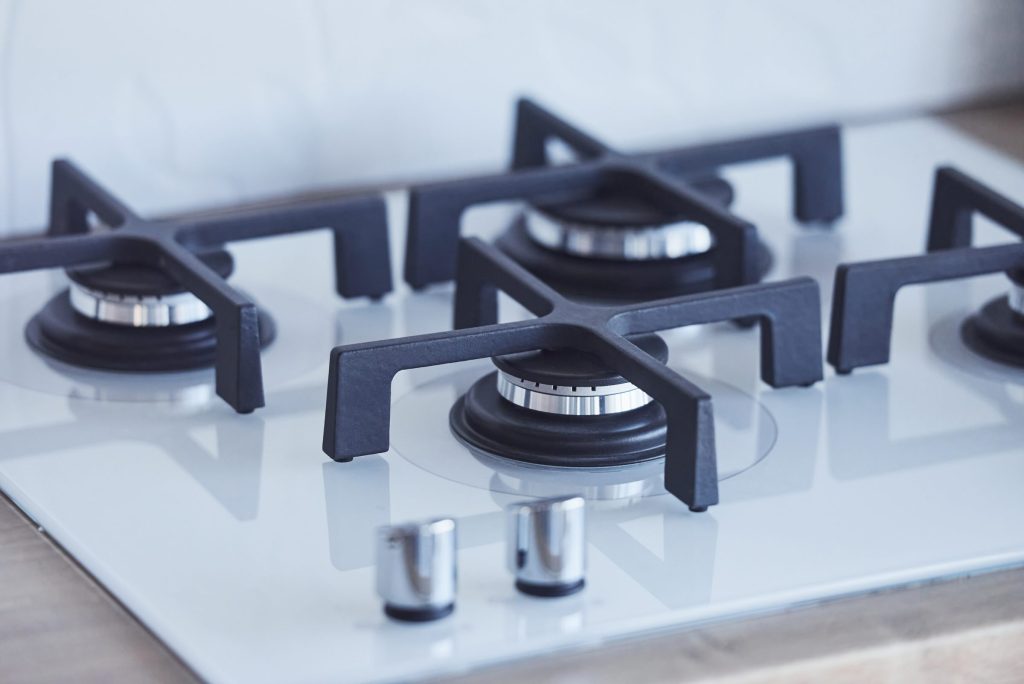 A white glass gas hob with cast grates and brushed knobs, seen from above