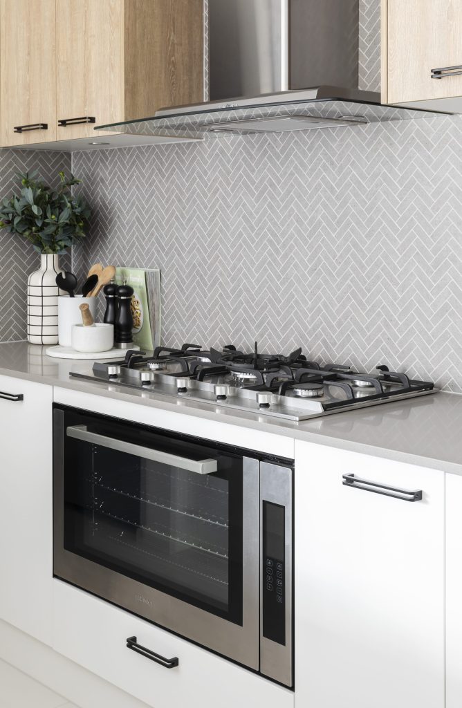 A stainless built-in oven under a gas hob in a grey kitchen