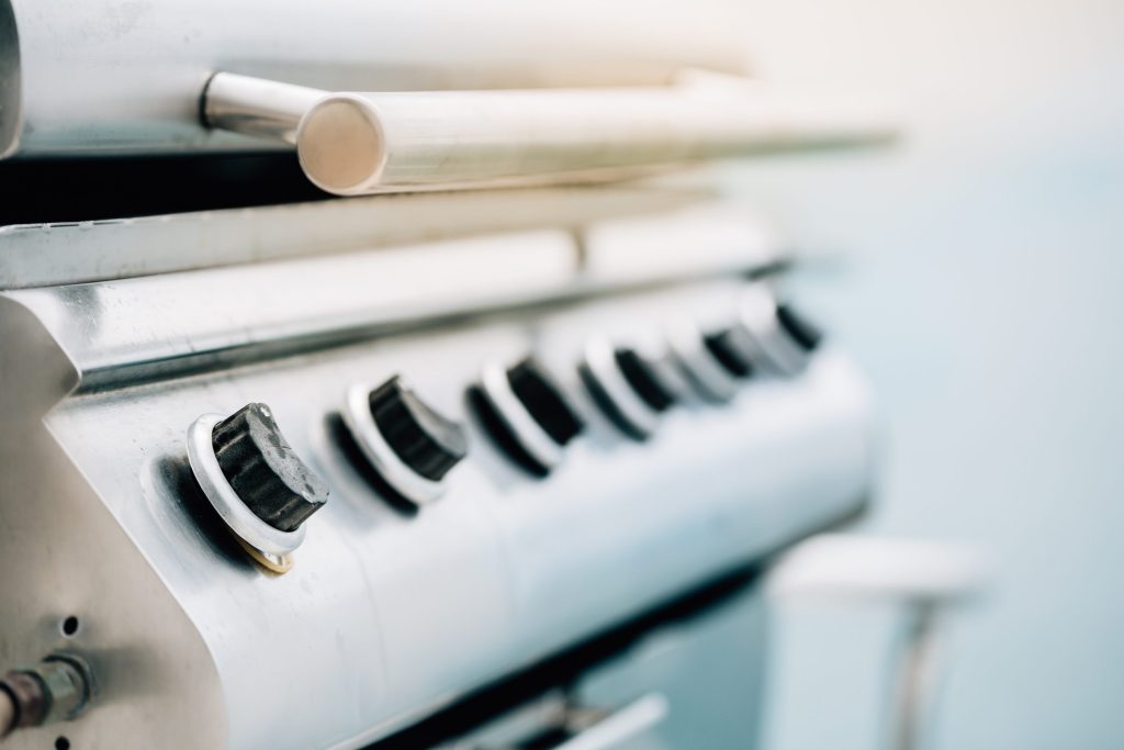 The row of control knobs along the front of a stainless gas grill