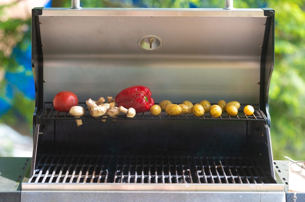 Peppers and onions on the grate of an open stainless gas grill