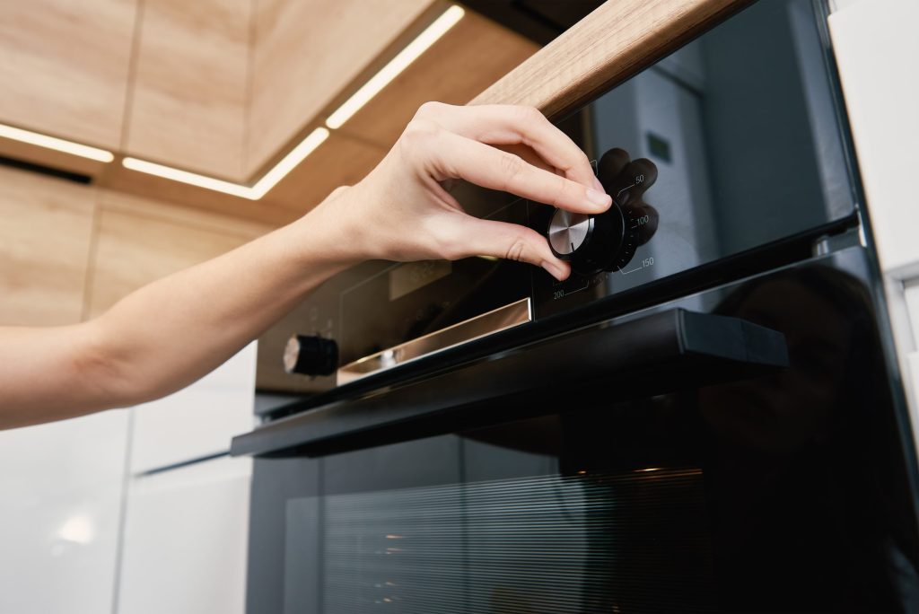 A hand turning the control dial on the fascia of a black built-in oven