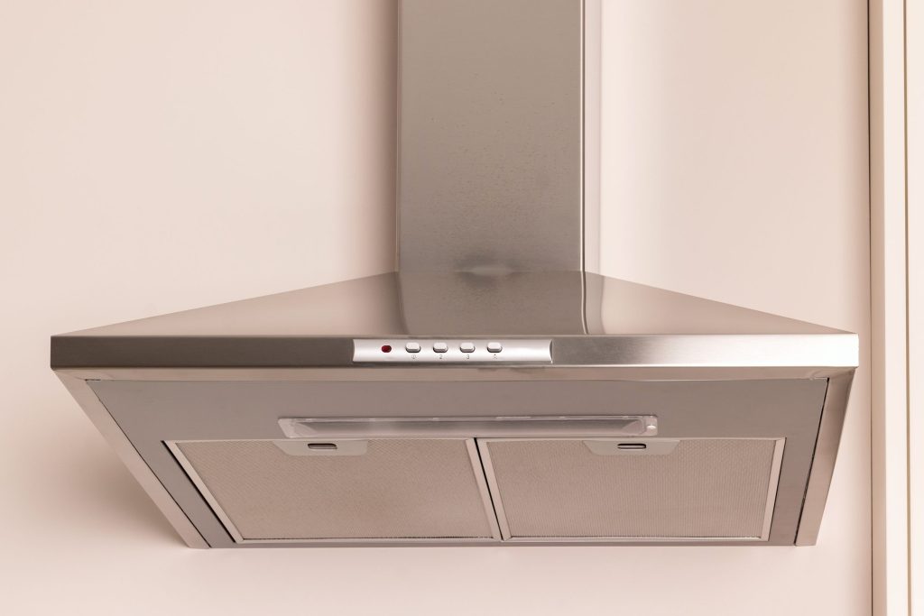 A stainless chimney hood against a plain wall, filters and controls in view