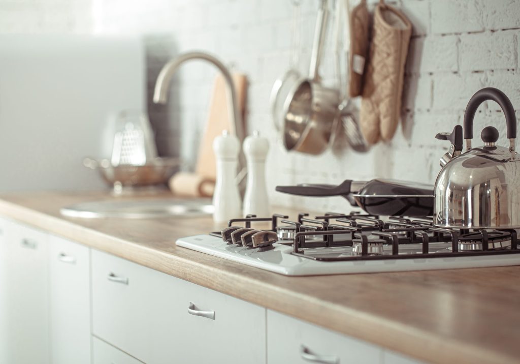 A gas hob on a wooden counter with a steel kettle beside it