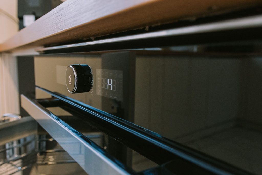 The fascia of a built-in oven under a wooden shelf, dial and display lit