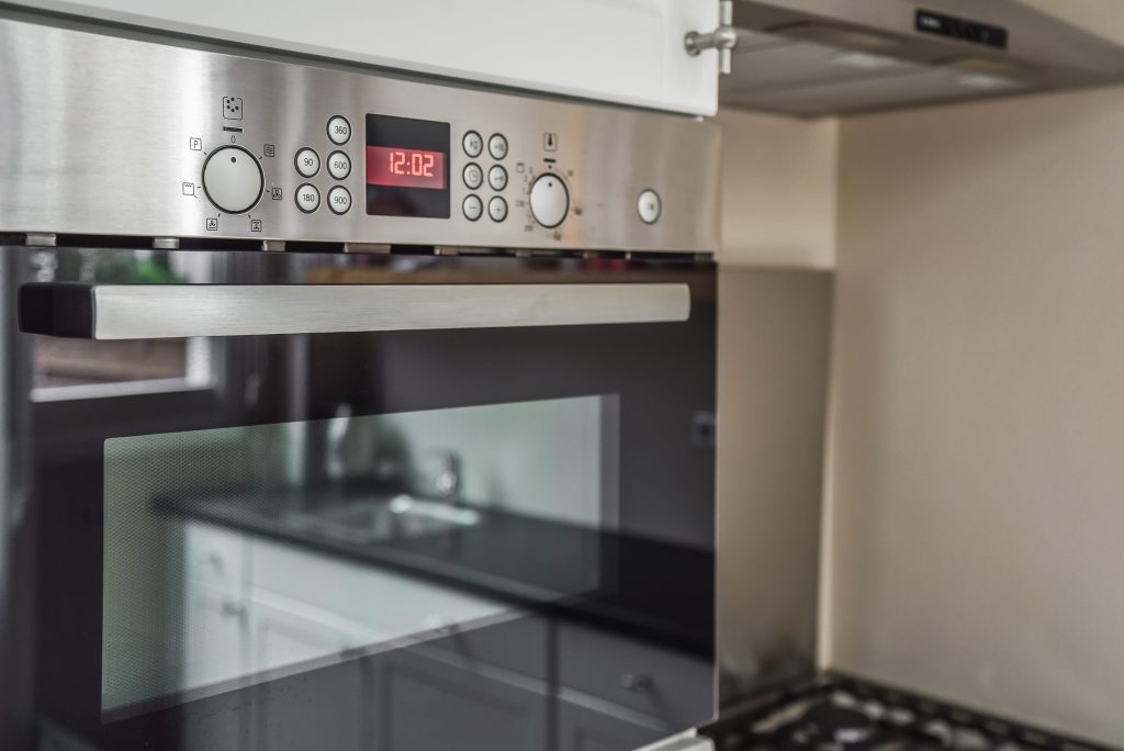 A stainless fascia with a lit clock above a black glass door, drawer handle across it