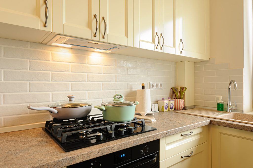 Two pans on a black hob set into a stone counter under wall units