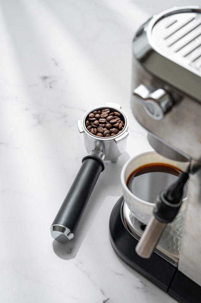 A portafilter of roasted beans beside a machine and a poured cup