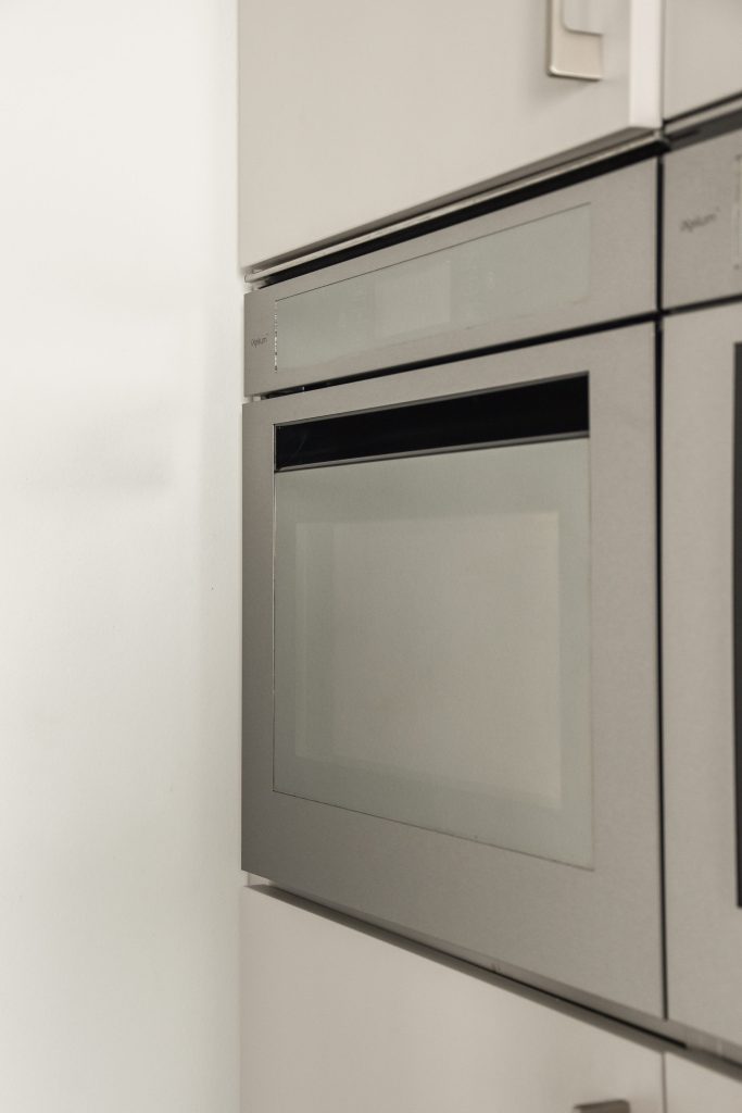 A slim built-in oven set into a white cabinet run