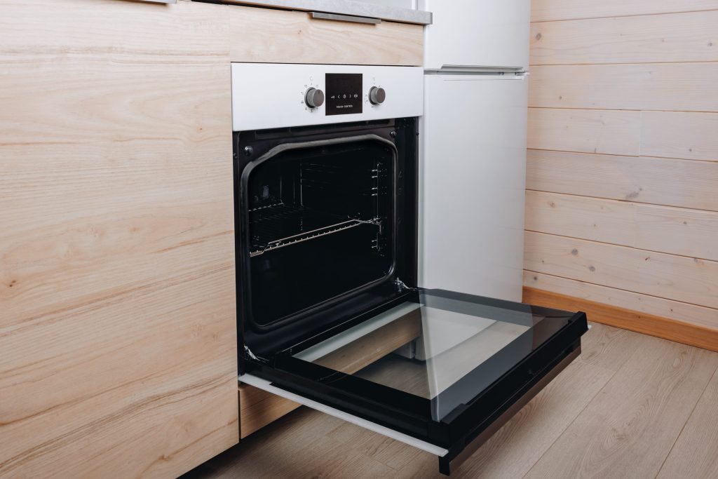 A white built-in oven standing open against a pale timber wall