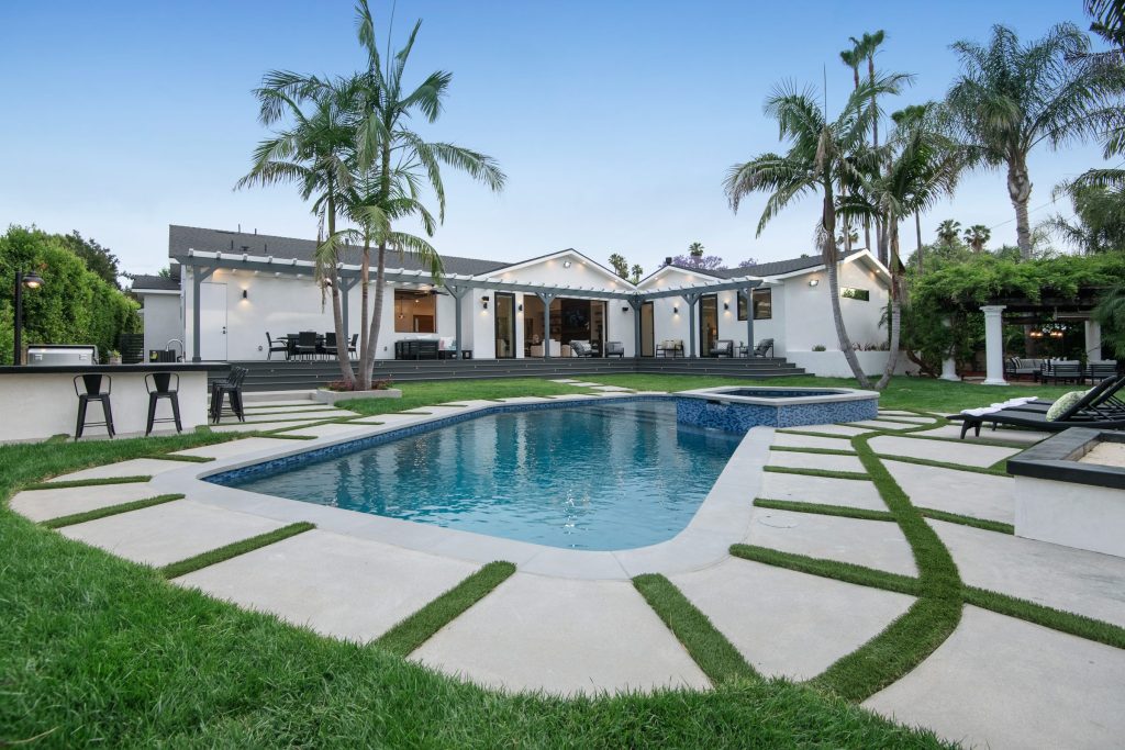 A pool set into a lawn behind a low house, palms along the boundary
