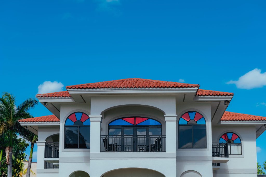 A white Mediterranean house with a red tile roof and arched balcony windows