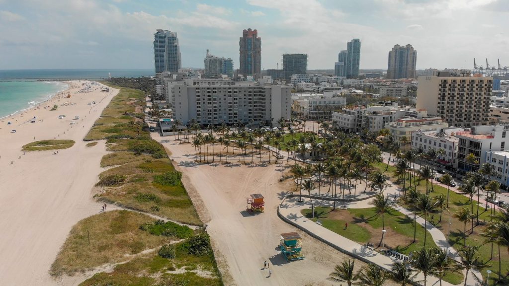 A wide beach with low blocks and towers behind it, from the air
