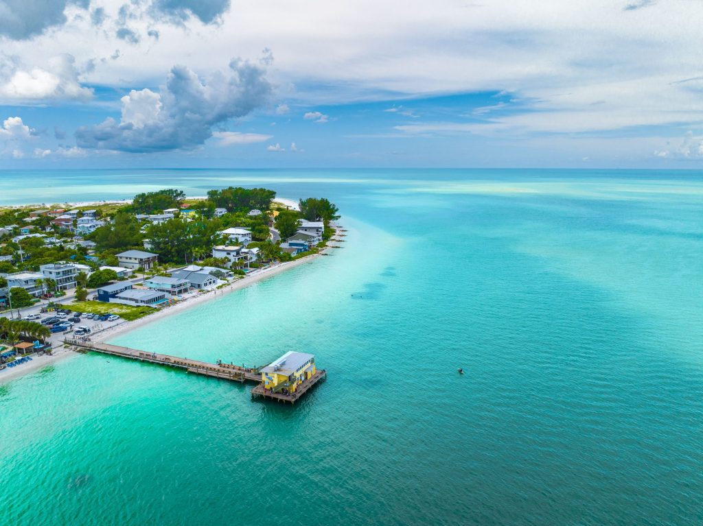 A low beach town on a point with a pier reaching into shallow water