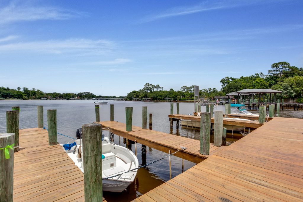 A timber dock on pilings with a small boat moored on a wide waterway