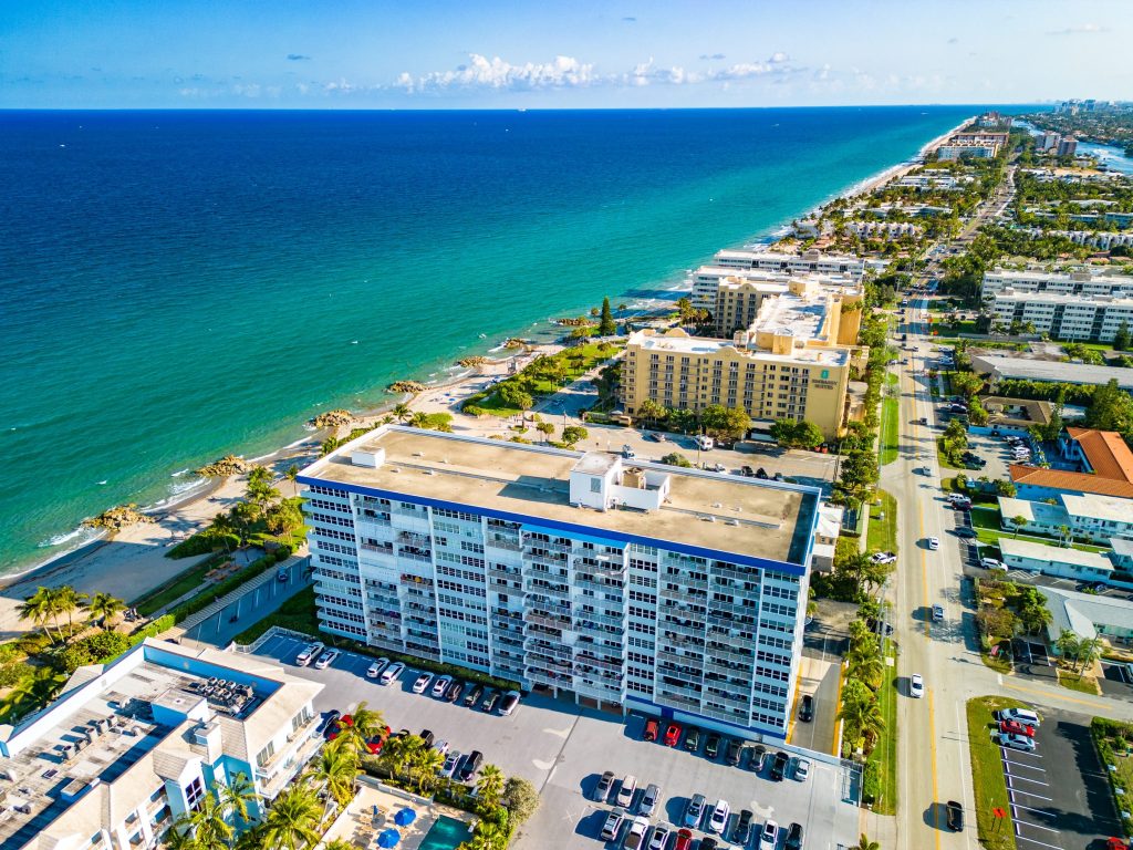 A coastline of low blocks and condo buildings along a turquoise beach, from the air