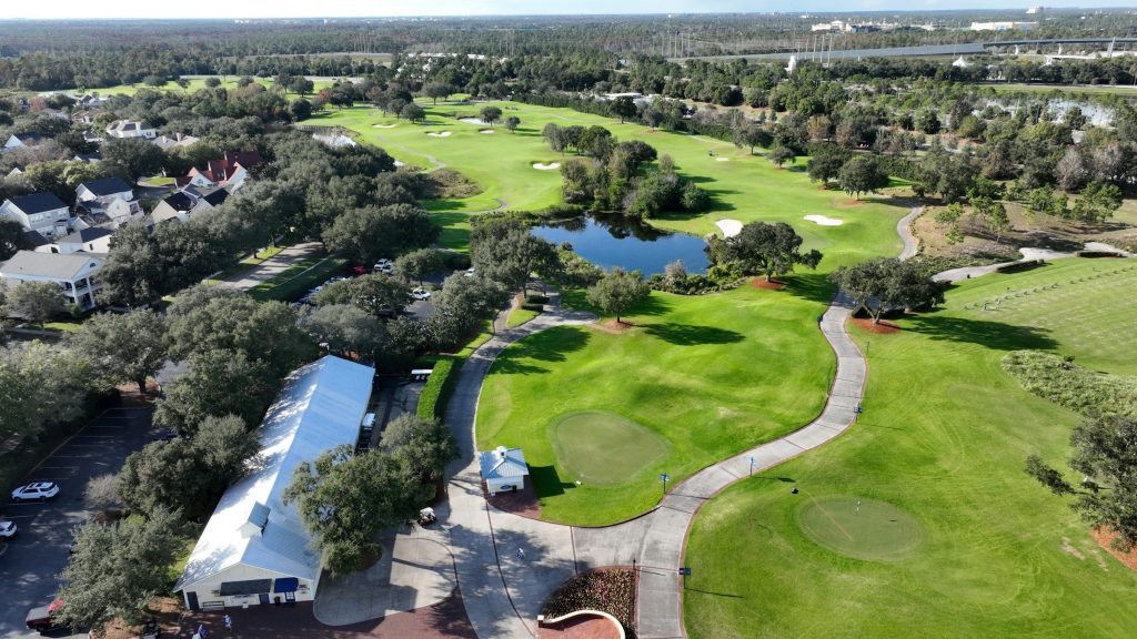Golf greens and a lake with a clubhouse drive beside them, from the air
