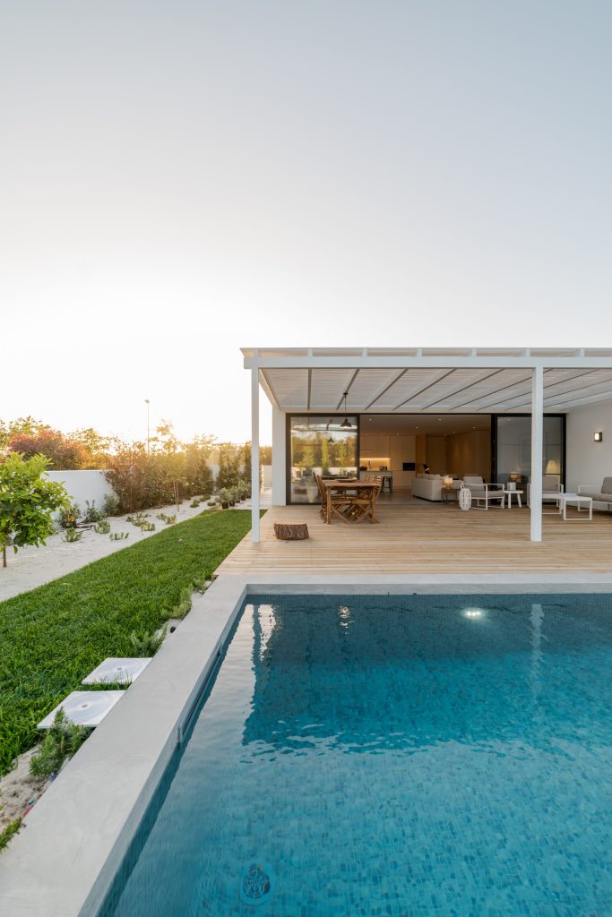 A pool and covered terrace beside a low house at dusk