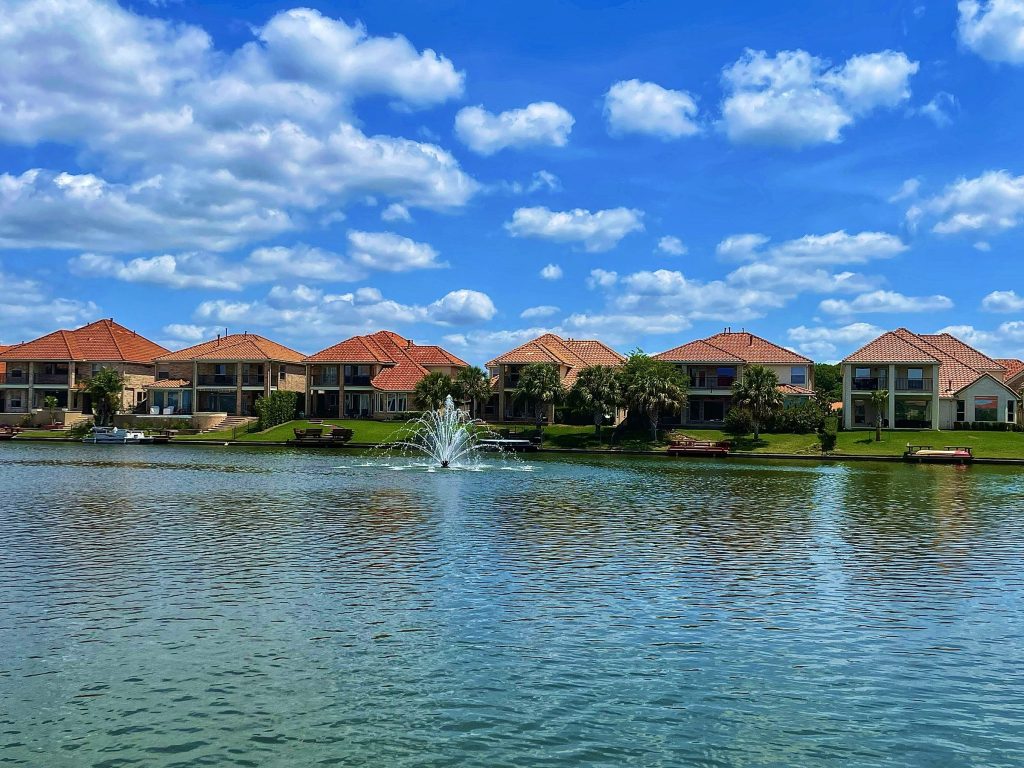 Lakefront houses with tile roofs behind a fountain on the water