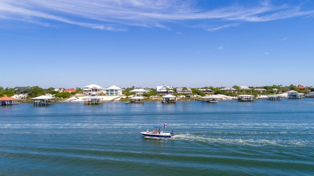 A boat crossing open water past low waterfront houses