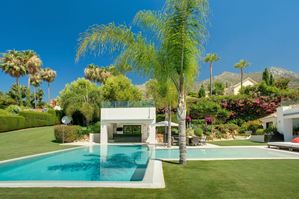 A pool terrace with palms and a pavilion above a lawn