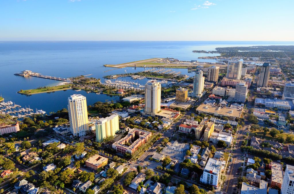 A waterfront district of towers beside a marina and a long pier, from the air