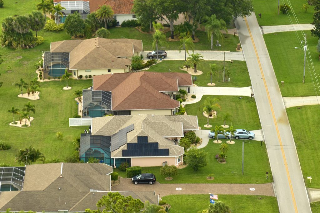 Tile-roofed houses with pool cages along a straight road, from above