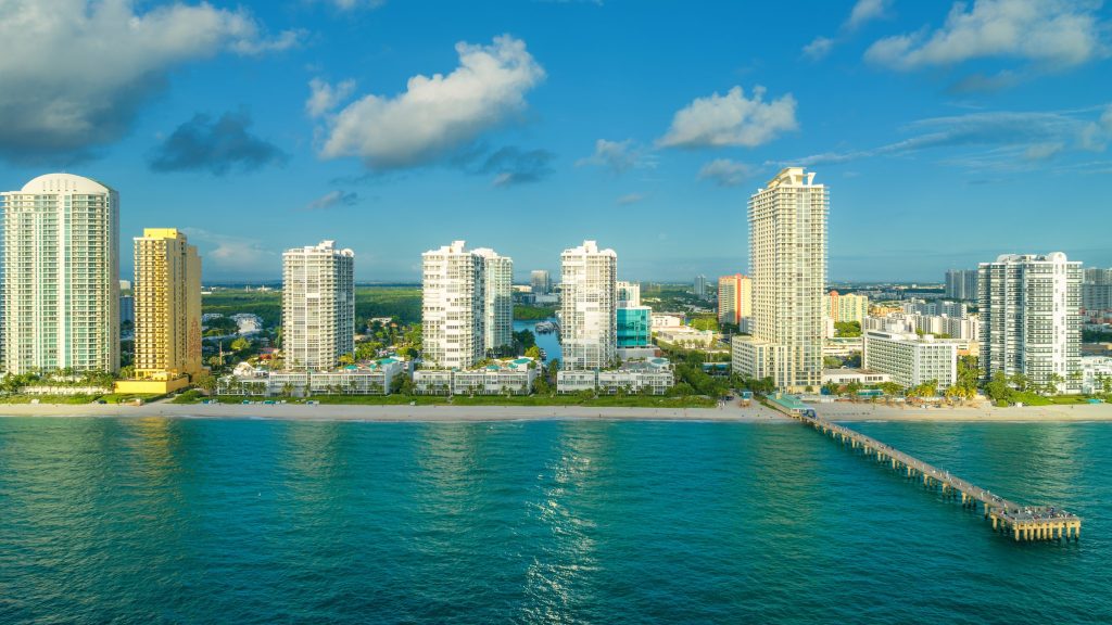 A row of oceanfront towers with a fishing pier beside them, from the air