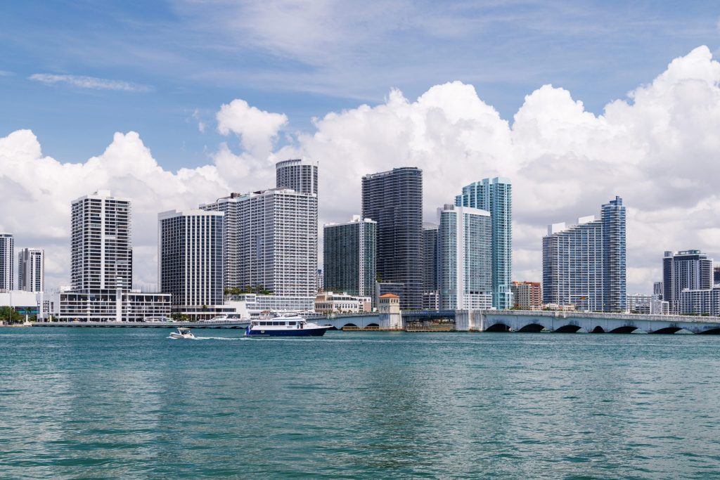 A row of towers along the water with a bridge in front