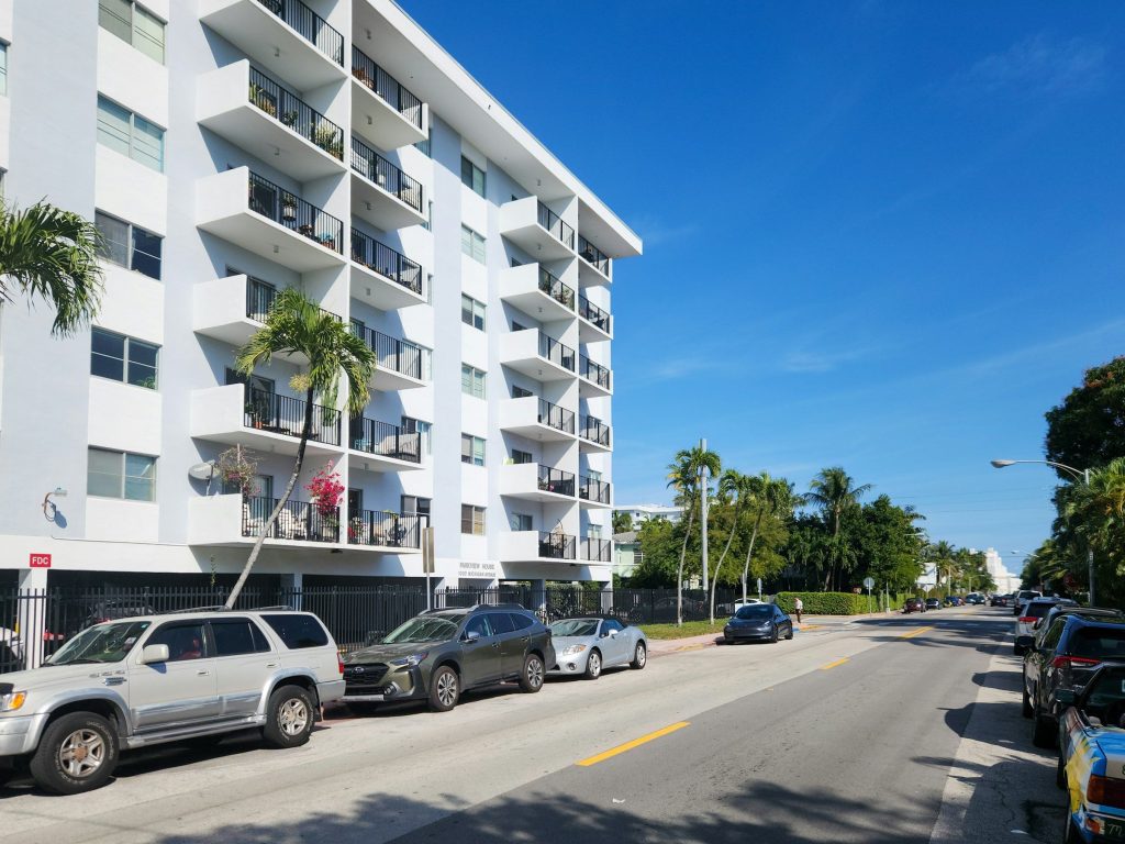 A white low-rise apartment block on a palm-lined street