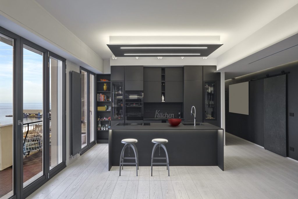 A total-black kitchen in a high-rise, an island with two stools and a wall of glass onto the ocean.
