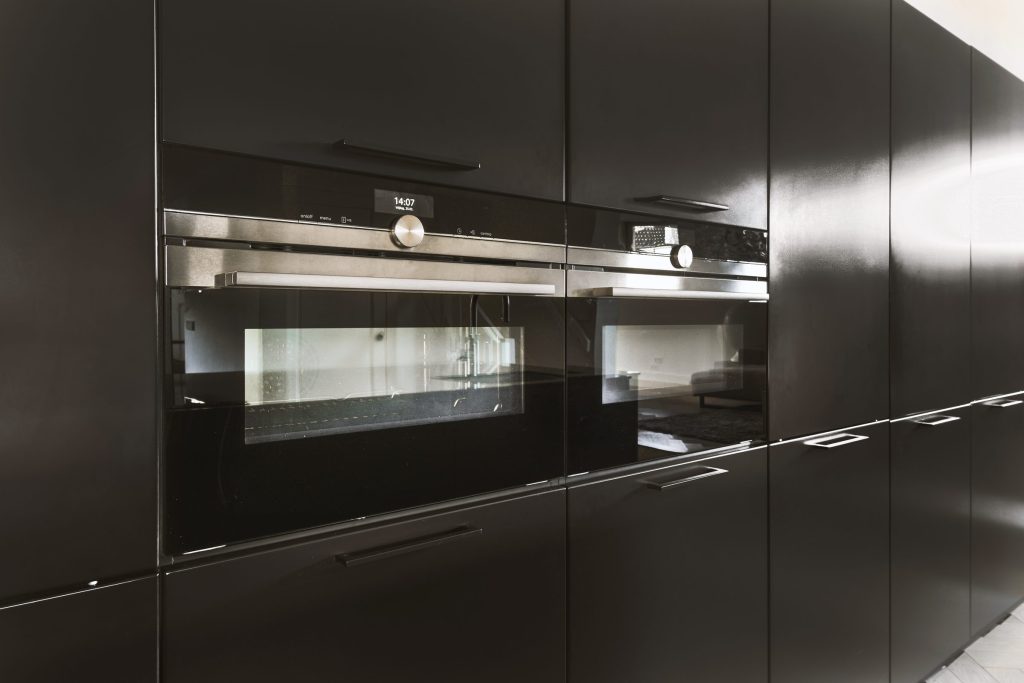 A run of tall black cabinets with two built-in ovens set into the column, their displays lit