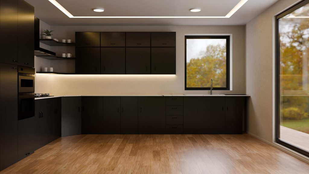 A black kitchen along one wall with a lit worktop, a wooden floor and a window onto the garden.
