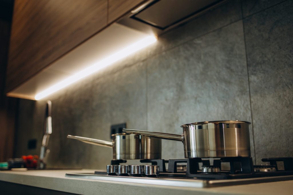 Steel pans on a gas hob in a dark kitchen lit by a strip under the wall units