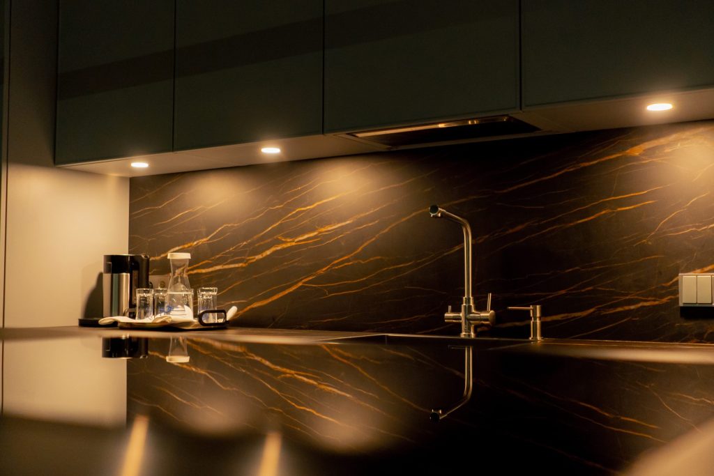 A dark counter against a gold-veined stone splashback, brass tap, glassware.