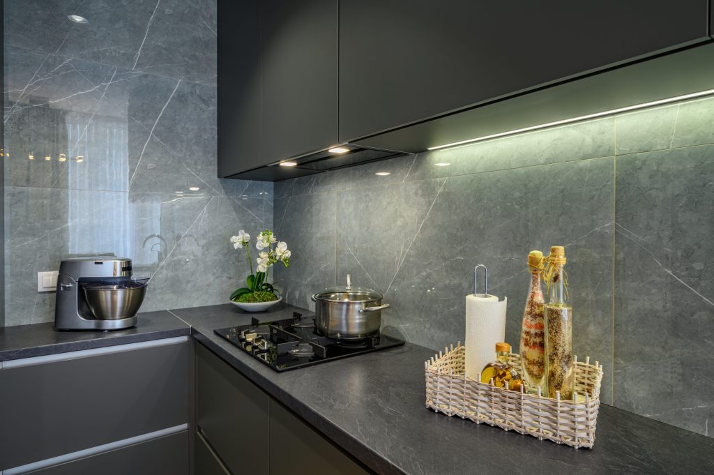A grey kitchen with a gas hob in a stone worktop and a stone splashback behind it