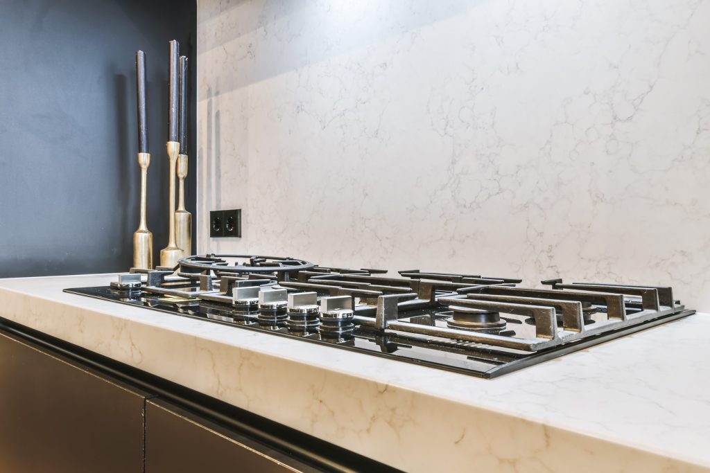 A stainless gas rangetop set into a pale marble worktop with a marble splashback behind it
