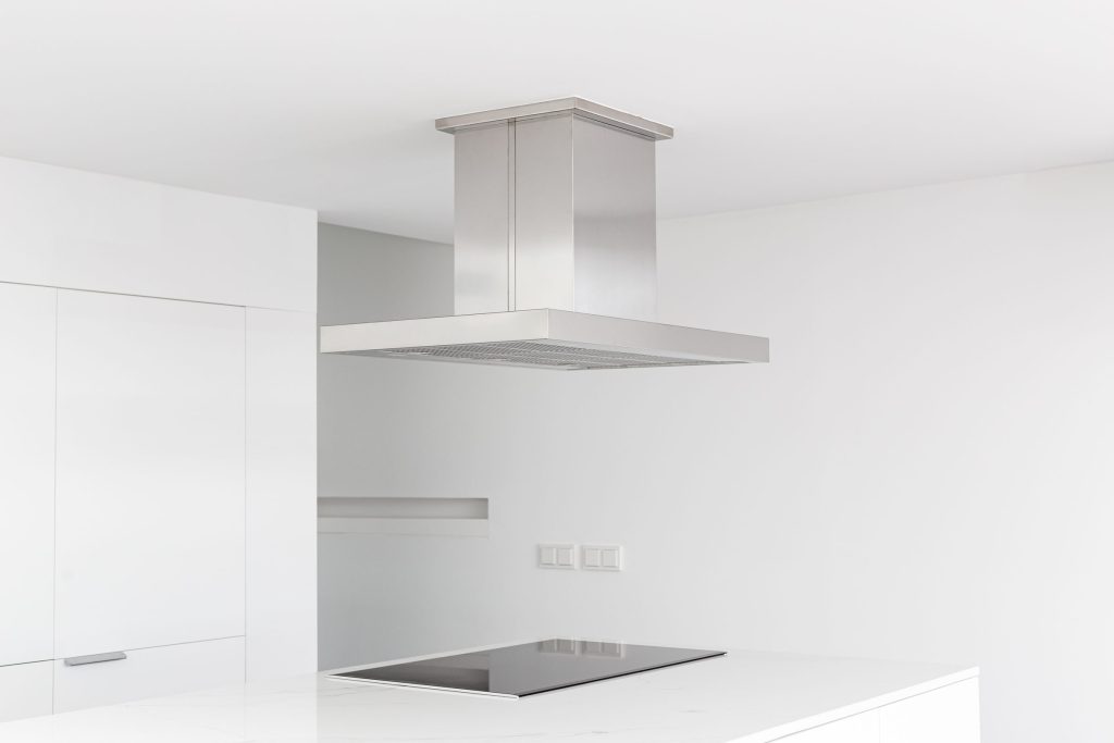 A minimal white kitchen with a stainless island hood above a flush induction cooktop.