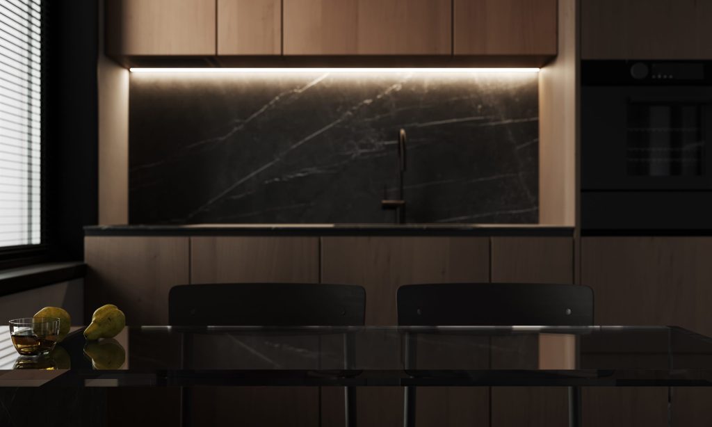 A dark kitchen in low light — pale wood units, a black marble splashback lit from beneath, a black oven at the right.